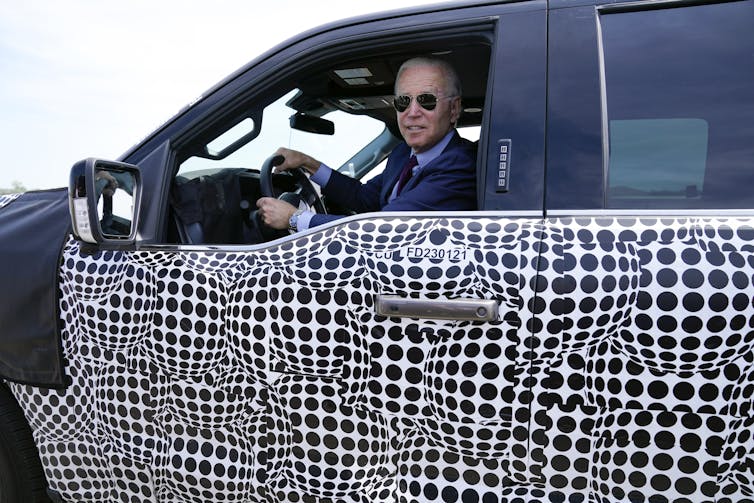 Biden speaks to reporters from the wheel of a new pickup truck.