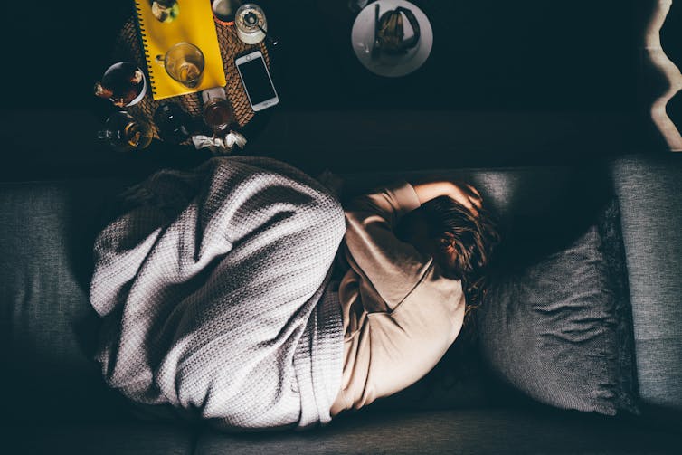 Person curled up on a couch, half-covered with a blanket