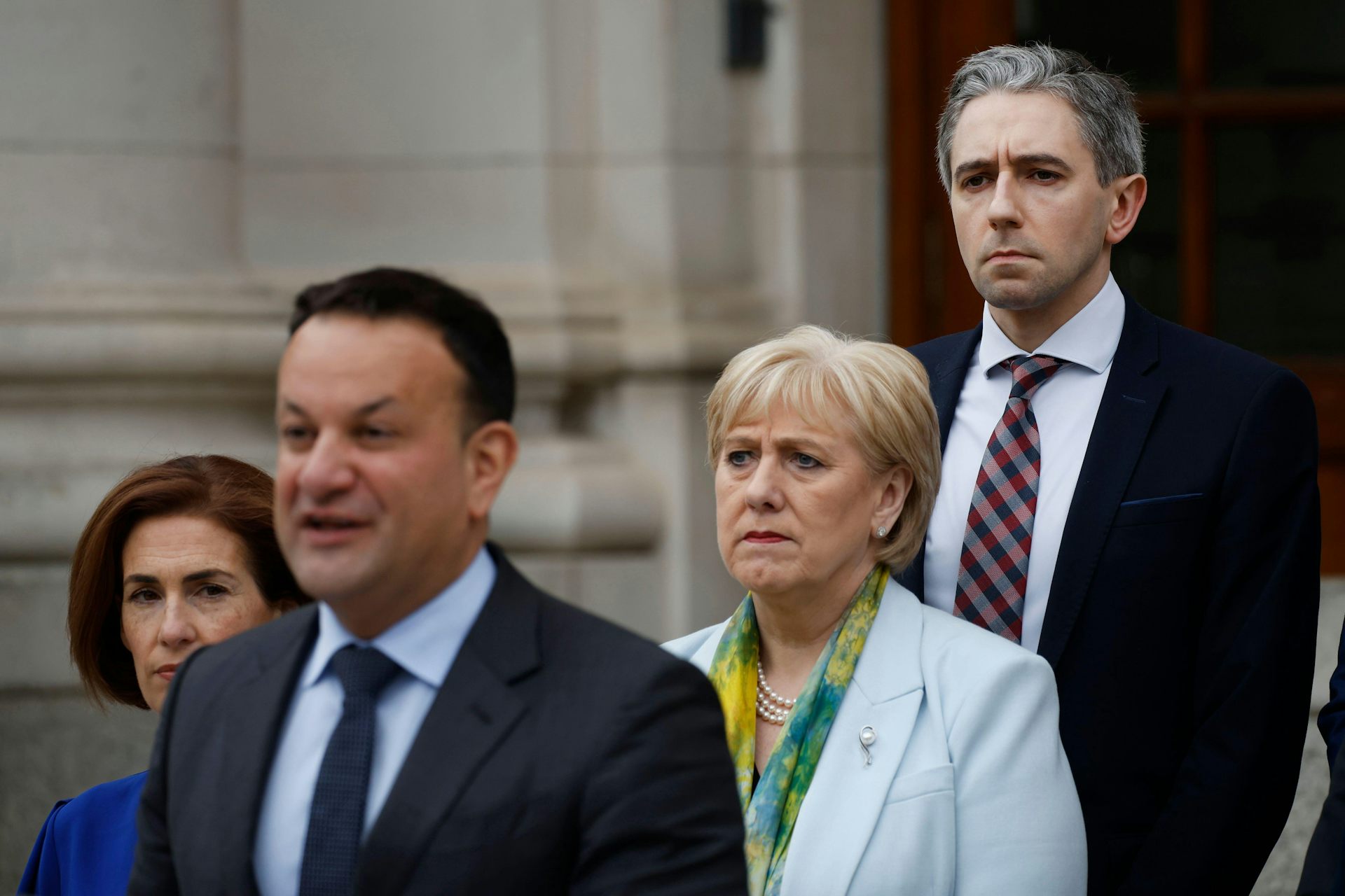 Simon Harris standing behind Leo Varadkar while the latter gives a speech.