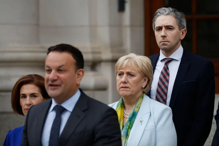Simon Harris standing behind Leo Varadkar while the latter gives a speech.