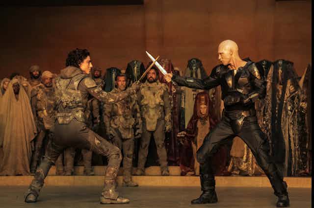 Scène de combat entre Paul Atréides et Feyd-Rautha Harkonnen dans Dune, deuxième partie. Les deux personnages croisent leurs dagues.
