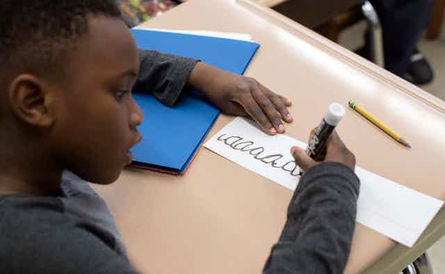 A student holding marker writing in cursive.