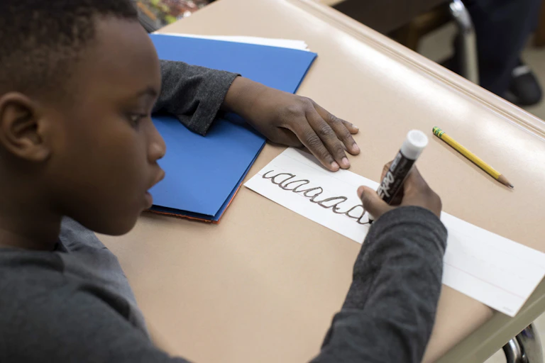 A student holding marker writing in cursive.
