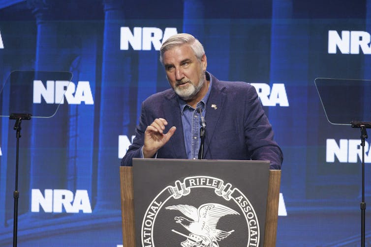 The governor of Indiana stands behind a podium during a presentation at an NRA event.