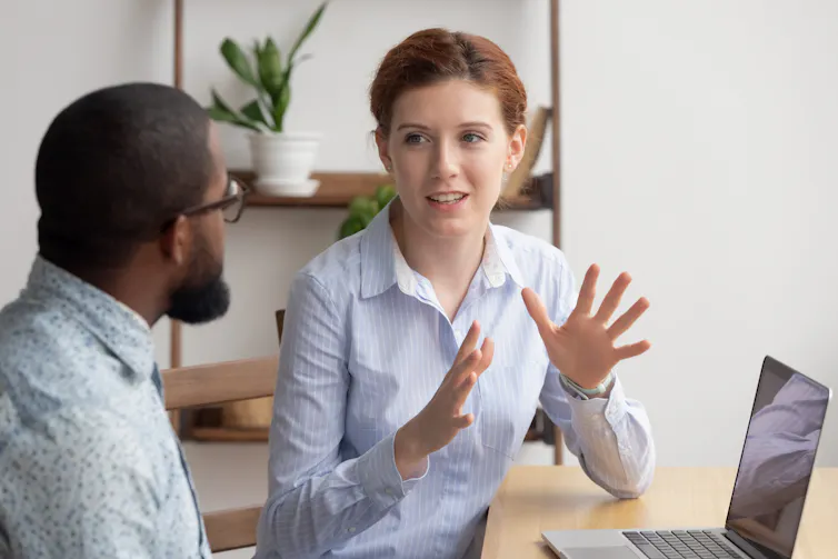 A woman gestures with her hands while speaking to a man who is seated beside her at a table