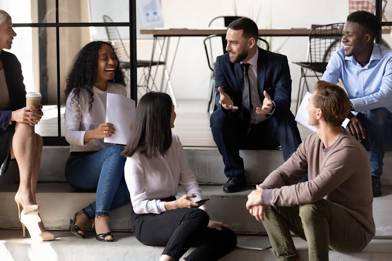 A group of people in workplace attire sit on concrete steps inside an office building