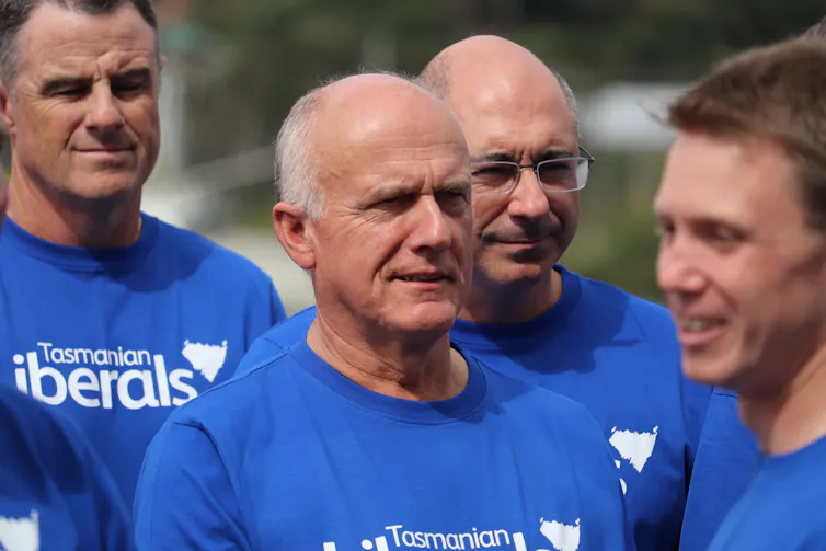 A man in a blue t-shirt stands among other men in blue t-shirts.
