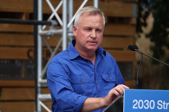 A man in a blue shirt speaking at a lectern