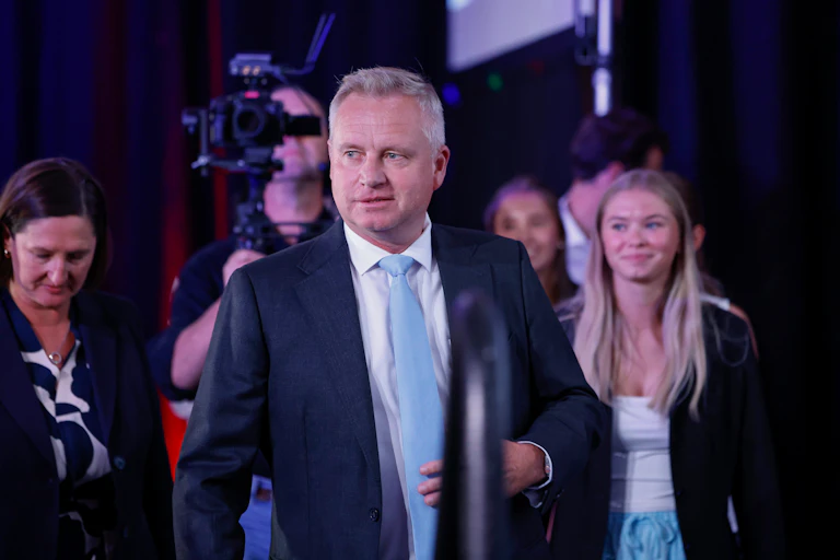 A man in a suit walks towards the stage, surrounded by family