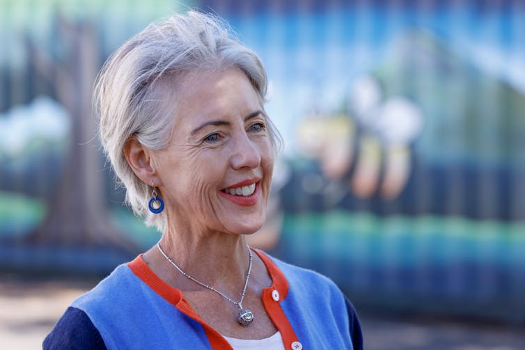 A woman in front of a glass window smiles across the camera