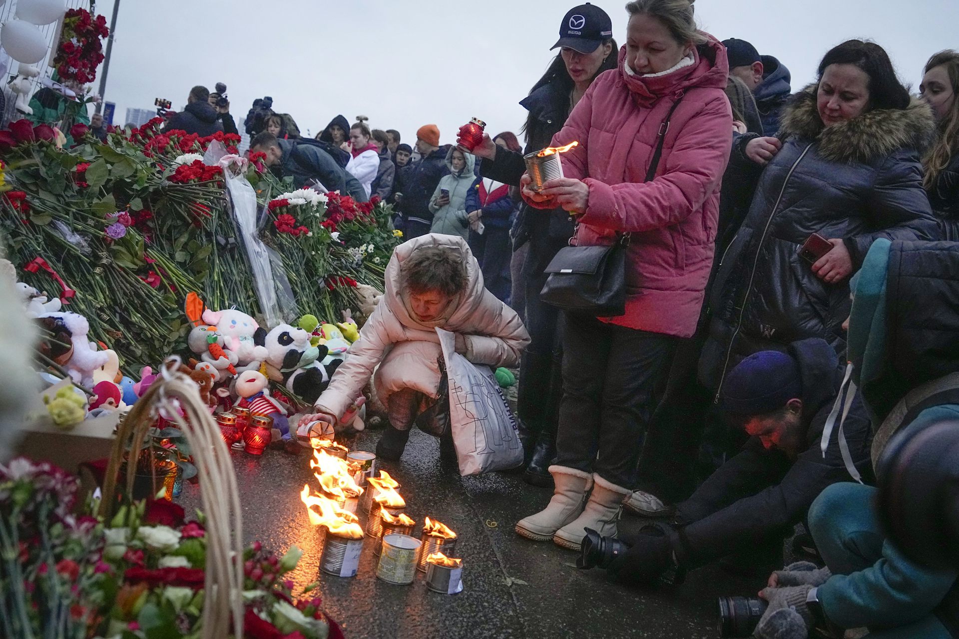 One woman kneels to light a candle while a crowd of other mourners look on.