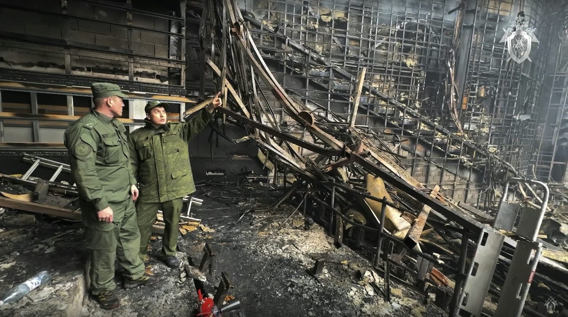 Two men in military gear examine a burned out concert hall.