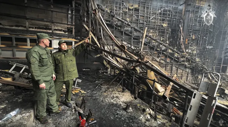 Two men in military gear examine a burned out concert hall.