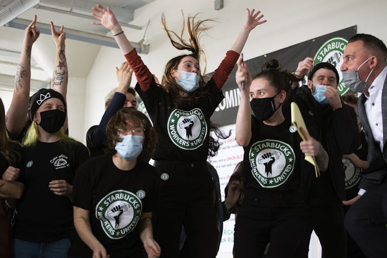 People in t-shirts that say 'Starbucks Workers United' t-shirts and face masks jump with joy.