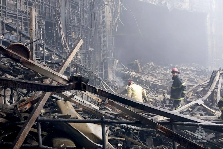Two people in hard hats stand amid rubble.