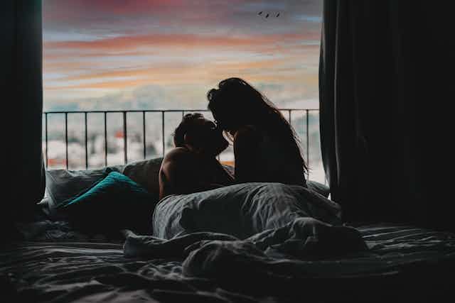 The silhouette of a couple almost kissing in bed