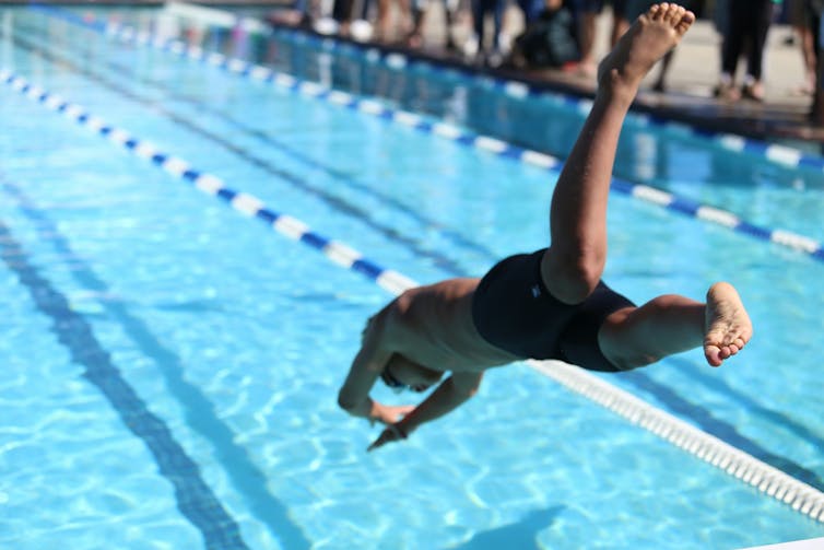 A young boy dives into a pool marked with lane ropes.