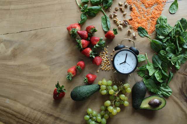 A clock on a table surrounded by fresh food.