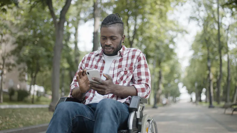 a man in a wheelchair outdoors looks at his phone