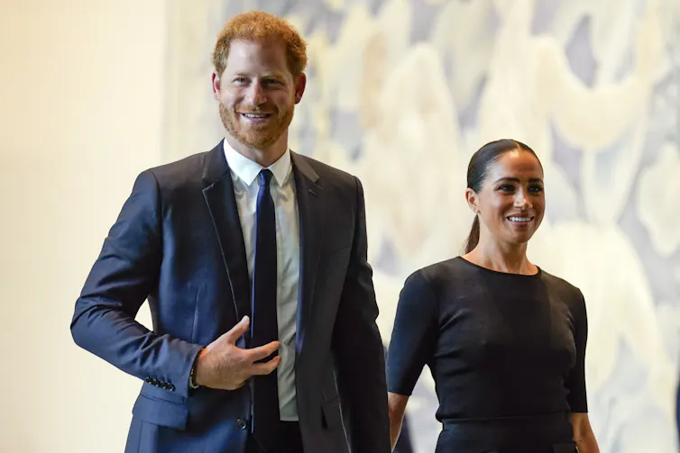 Prince Harry, wearing a suit, walks hand in hand with his wife, Meghan