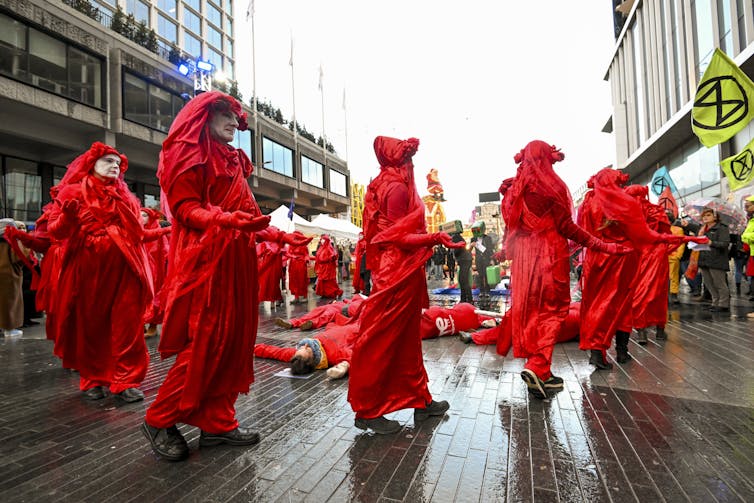 People in red costumes protest outside the headquarters of an oil company.