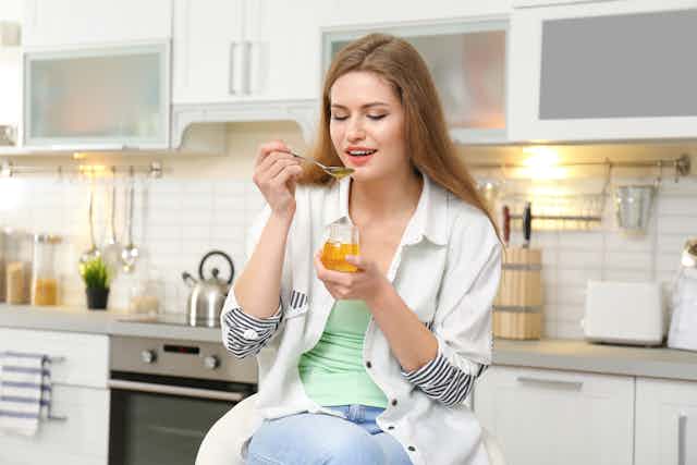 A woman eats a spoonful of honey in her kitchen.