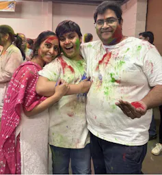 Three people in white with coloured powder on their clothes and bodies.