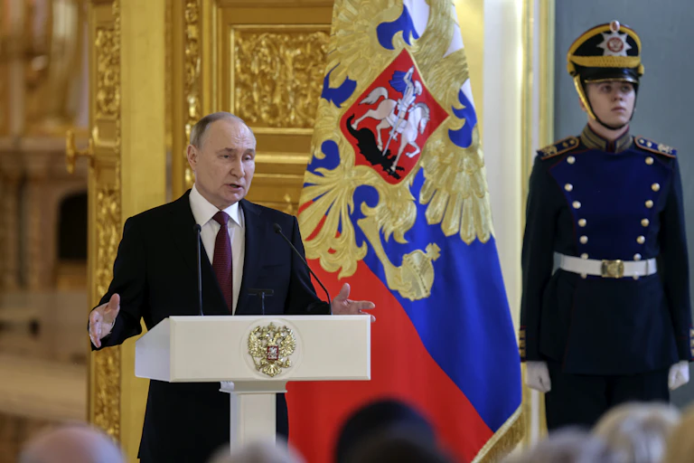 Russian president Vladimir PUtin delivers remarks from a lectern flanked by a soldier in ceremonial unifform.