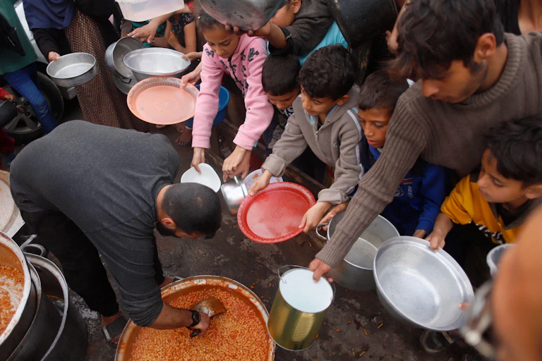 Palestinian children hold out their bowls to receive food.