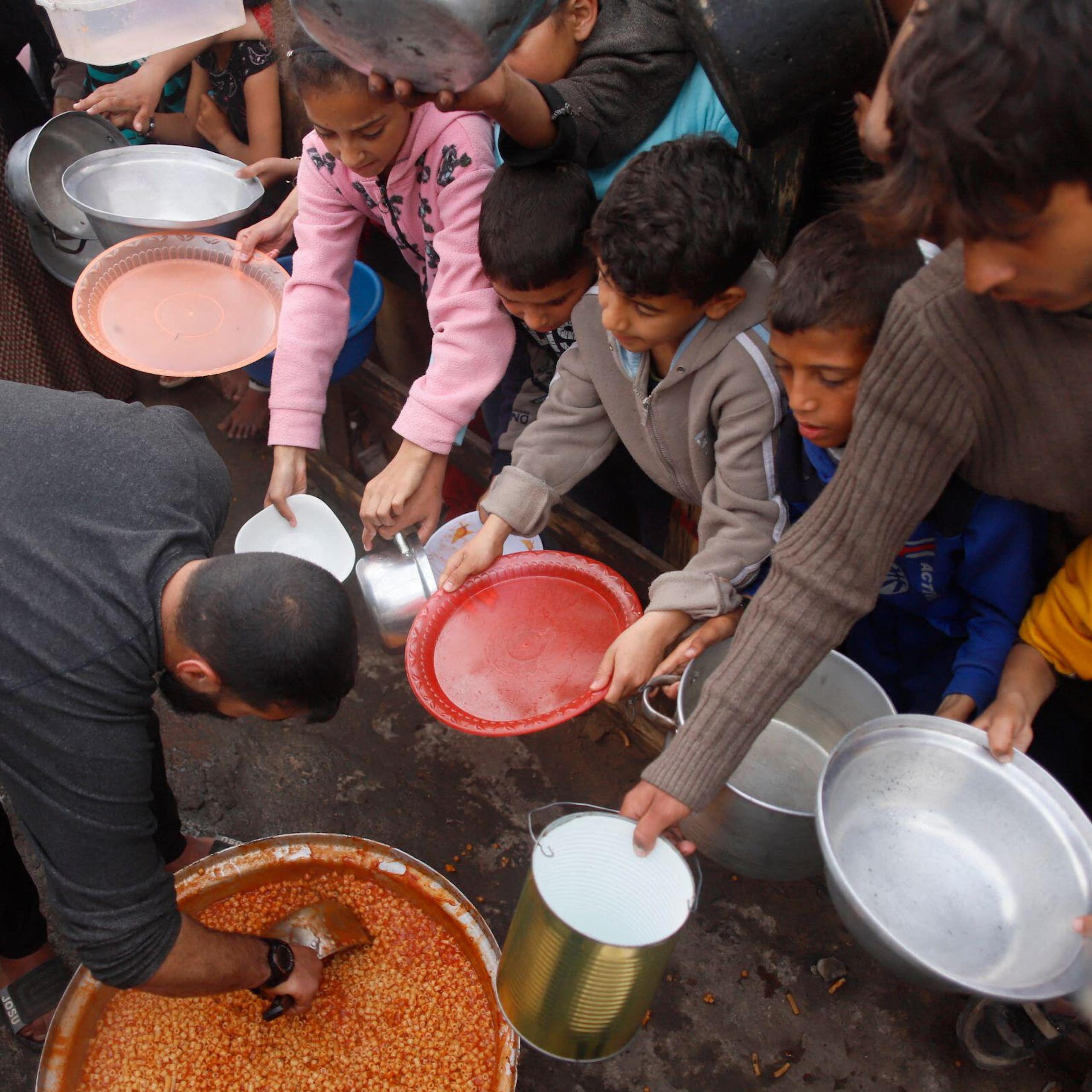 Palestinian children hold out their bowls to receive food.