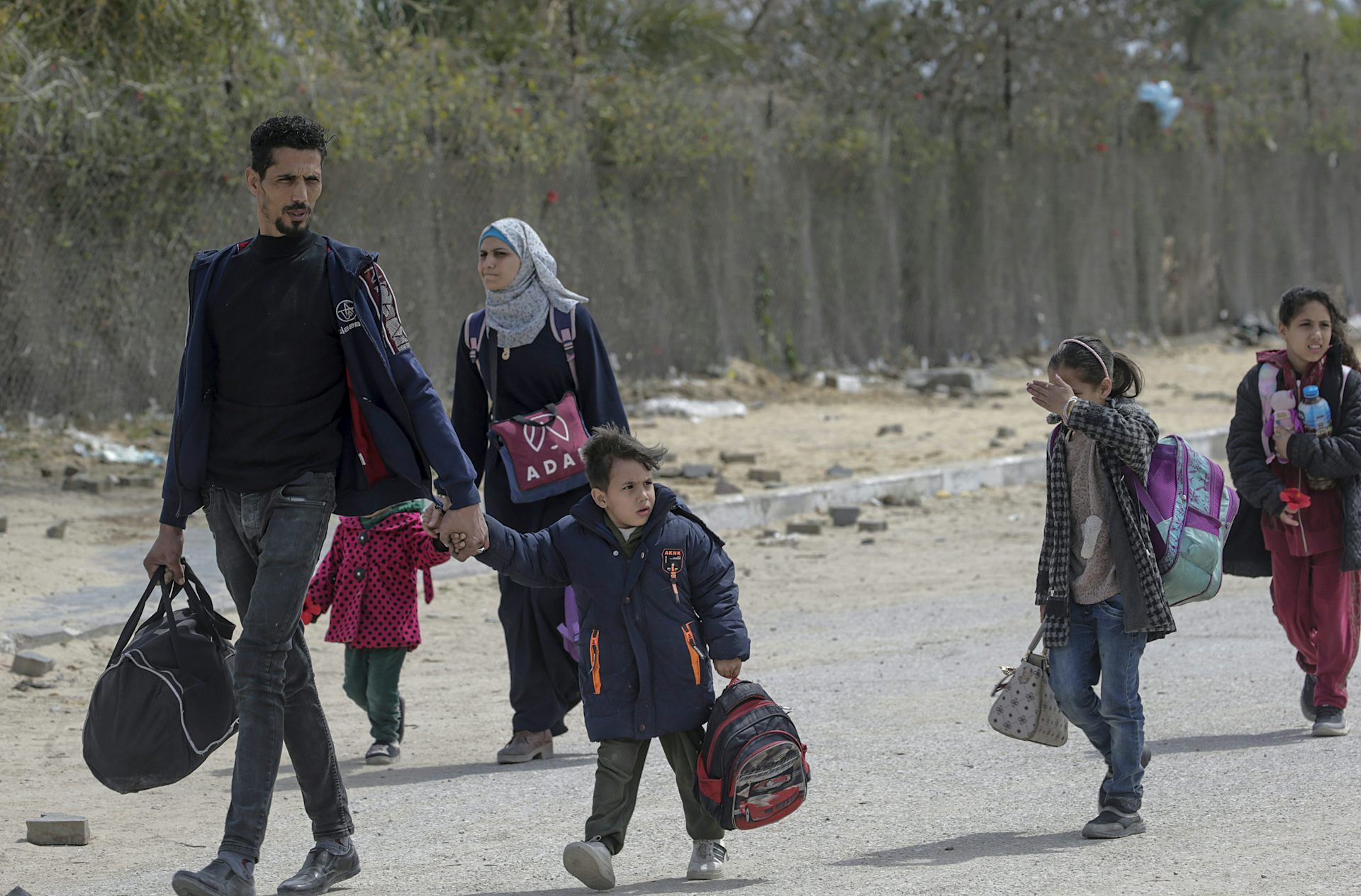 A Palestinian mother, father and three children carry their belongings down a road.