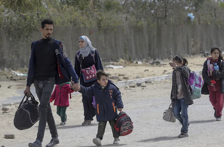 A Palestinian mother, father and three children carry their belongings down a road.