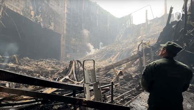 Un homme en treillis militaire observe un immeuble en ruines