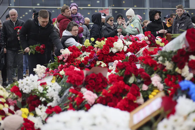Des personnes sont attroupés devant un amoncellement de fleurs