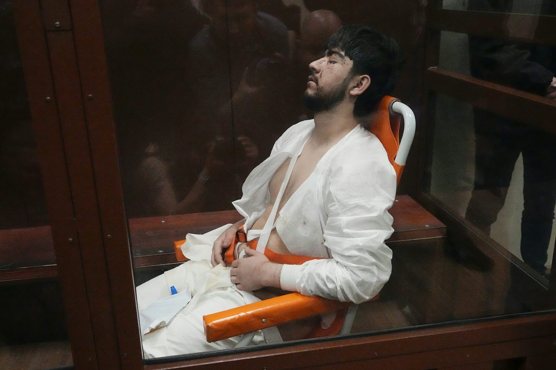 Un homme vêtu d’un survêtement blanc git, inconscient, sur une chaise