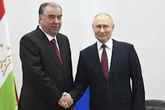 Two men in dark suits shake hands.