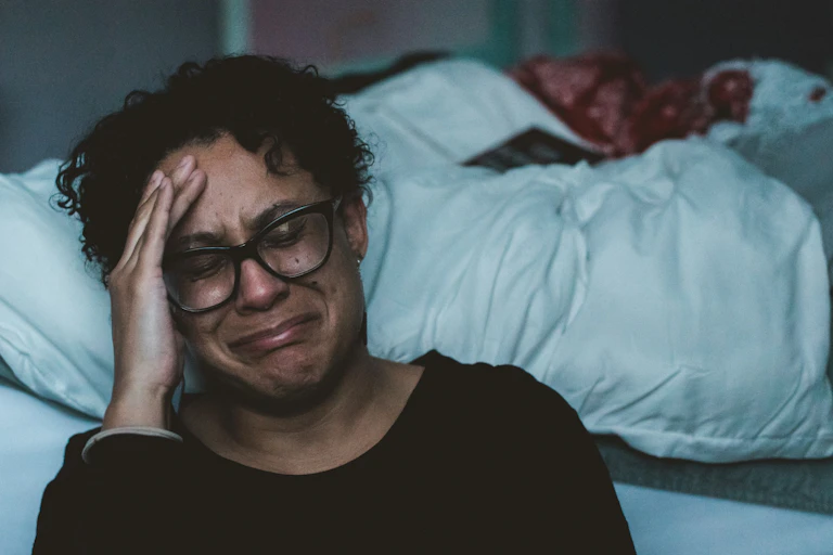 Anguished person sits at their bedside, their hand holding their head.