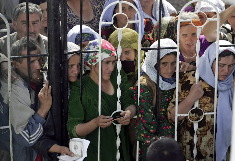 Women in kerchiefs press against a metal fence.