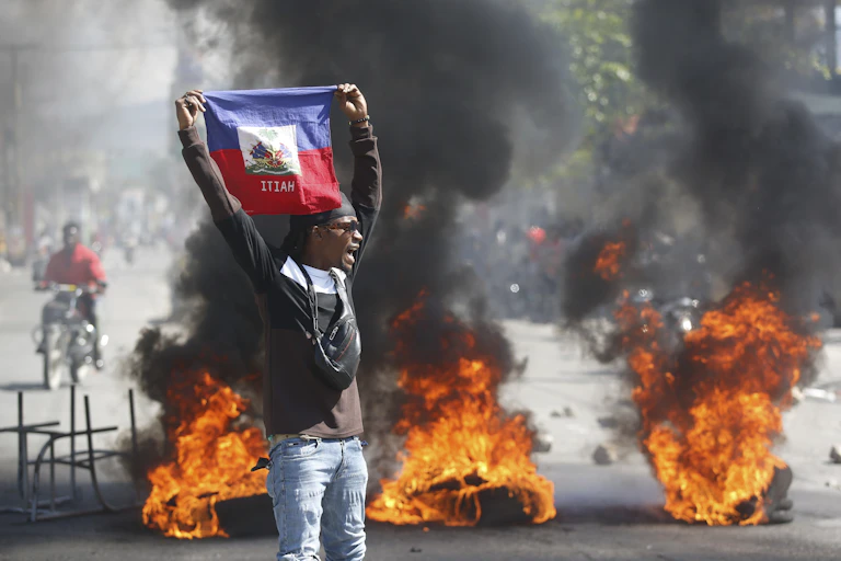 A man waves a flag. Smoke and fire in the background.