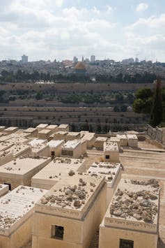 Beige stone boxes sit on the ground in rows, with a building with a golden roof in the distance.