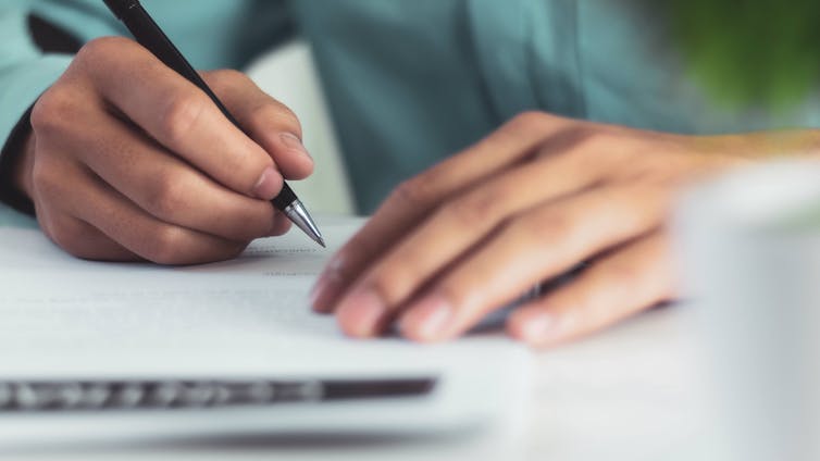 A photo of a person's hands holding a pen and writing on paper.