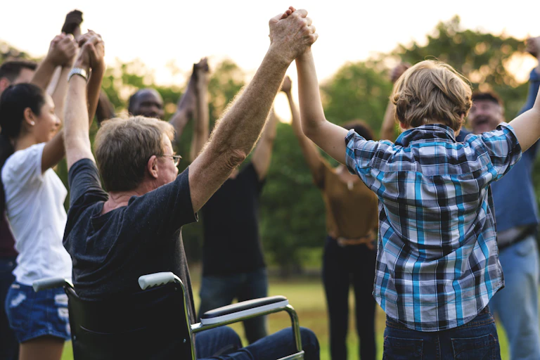 A circle of people in a park holding hands.