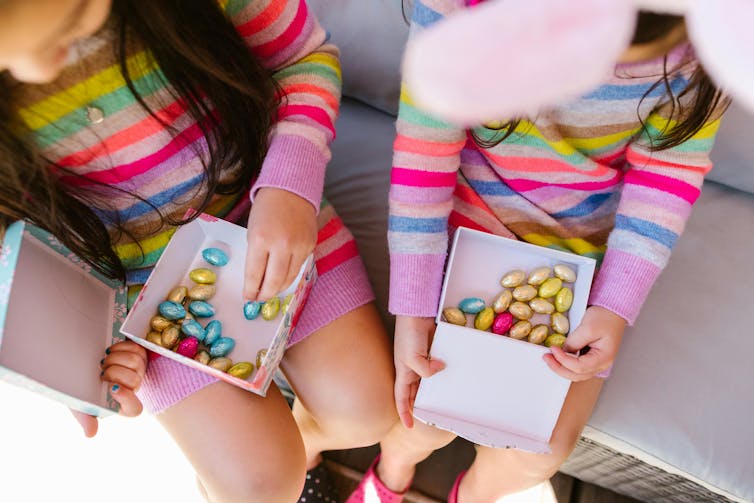 Two young children hold boxes containing small, chocolate eggs in foil wrapping.
