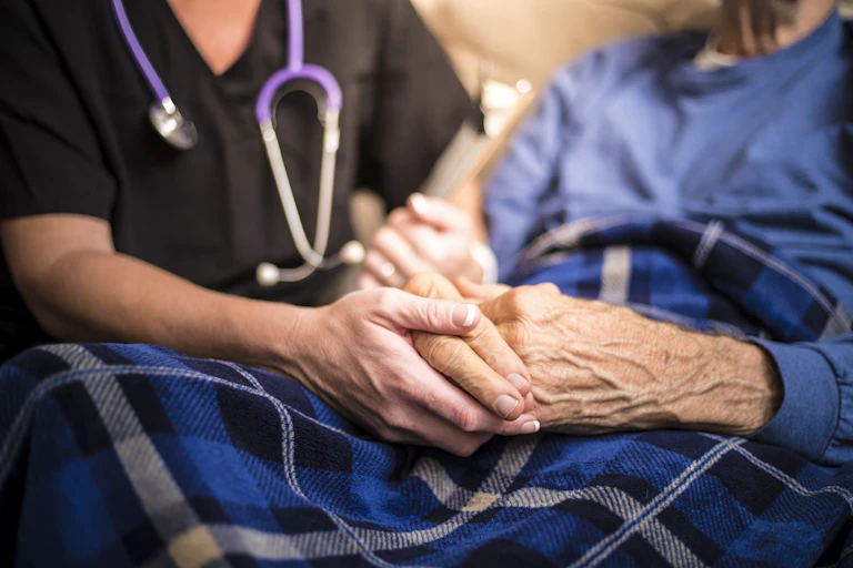 Hospice nurse holds the hands of an elderly male patient.