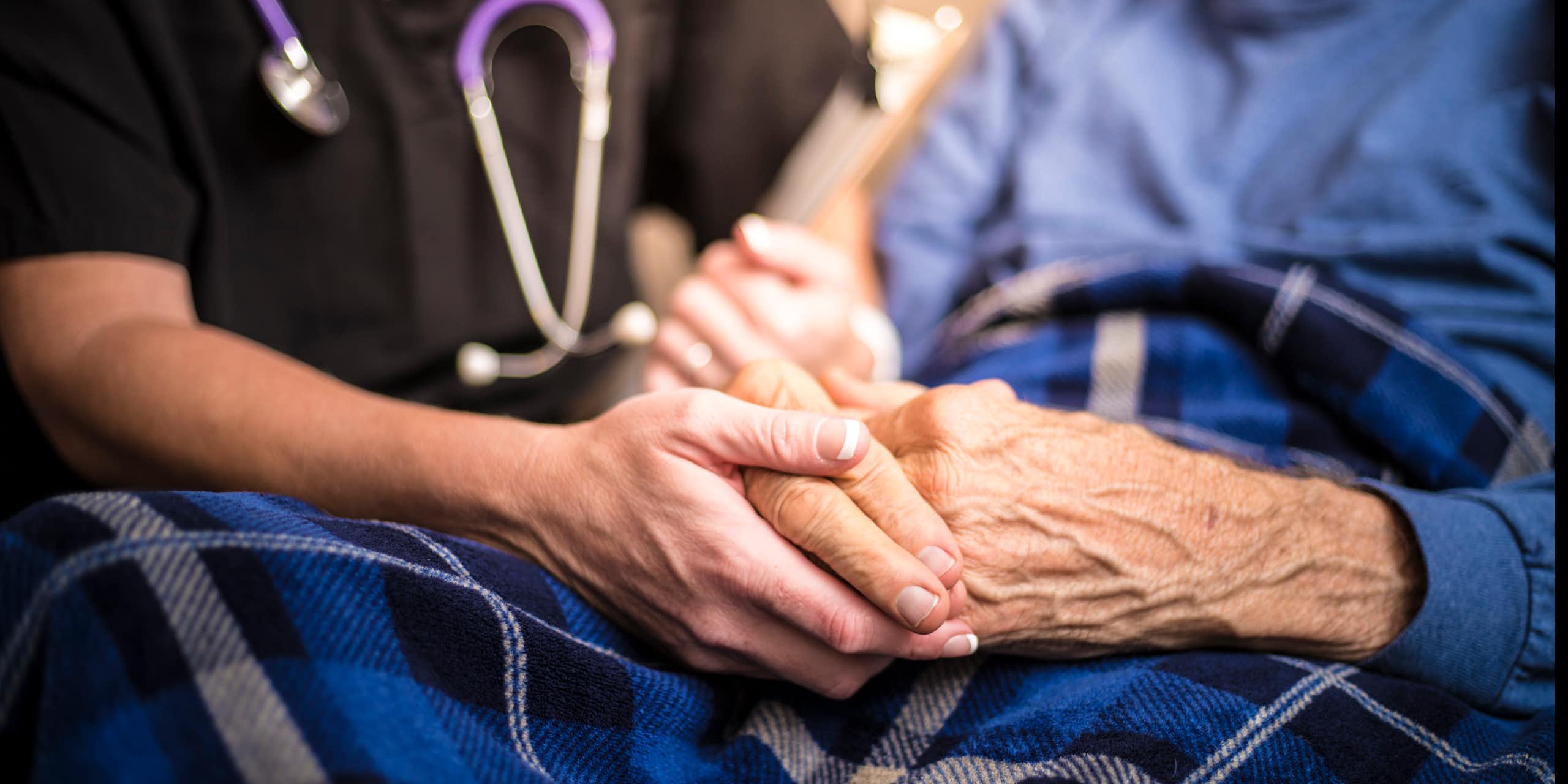Hospice nurse holds the hands of an elderly male patient.