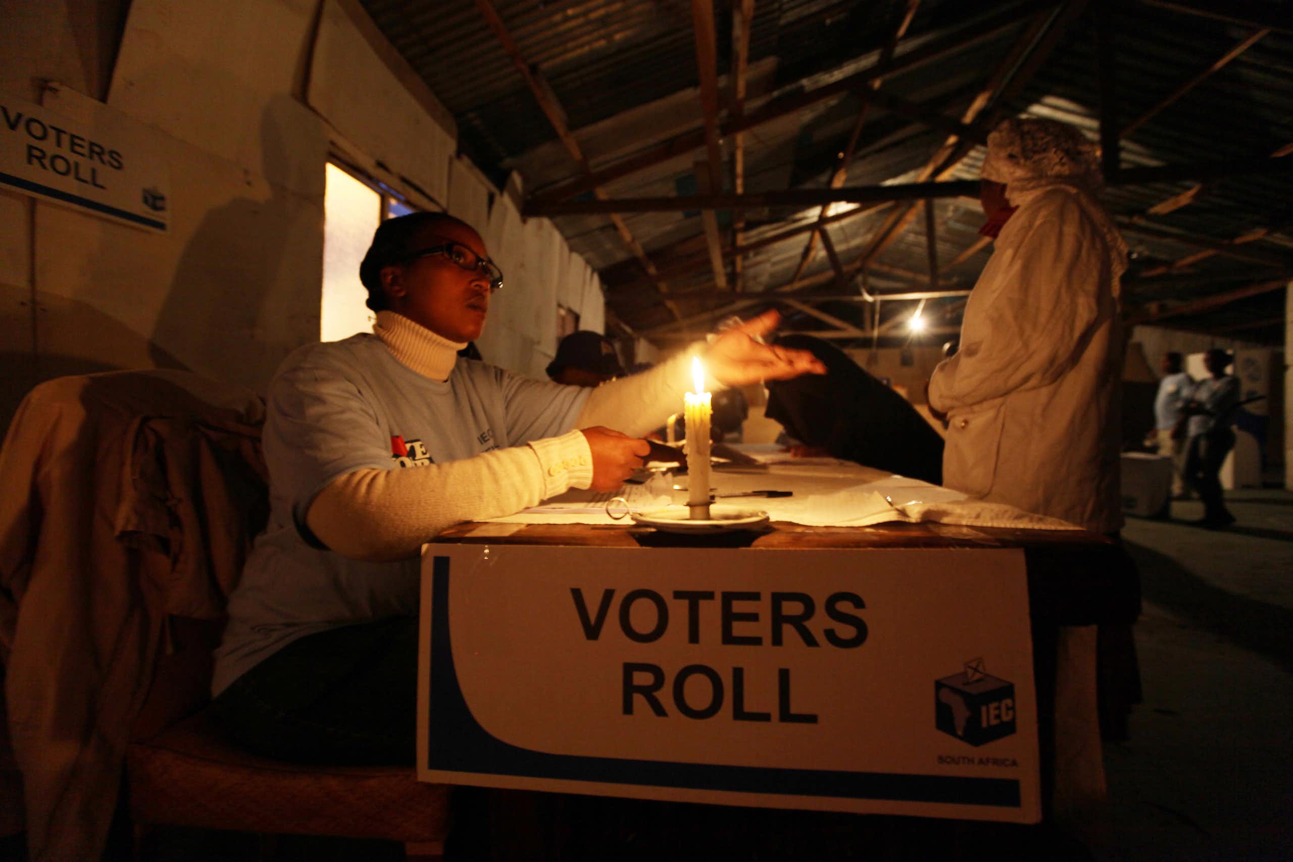 A voter casting a ballot at a voting table in the dark where there is only a candle