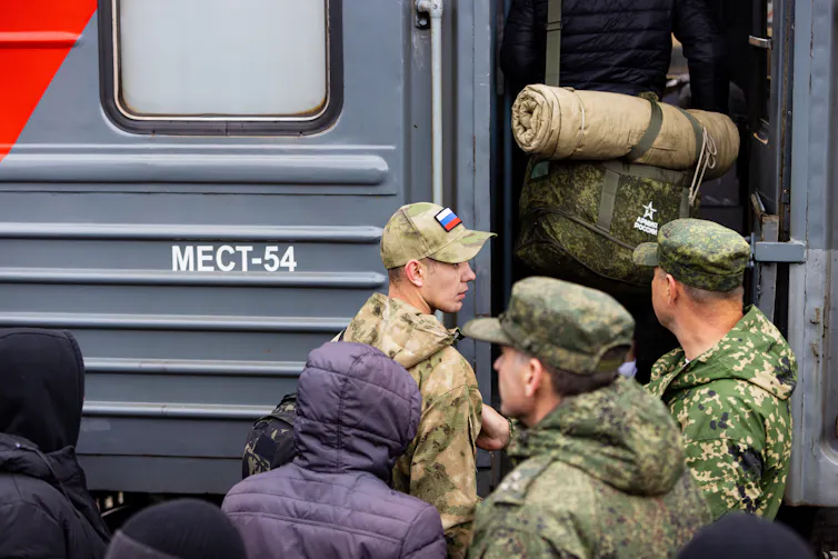 A man dressed in army attire with a cap featuring the Russian flag boarding a train.