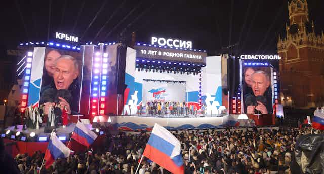 Vladimir Putin on a stage addressing a large crowd.