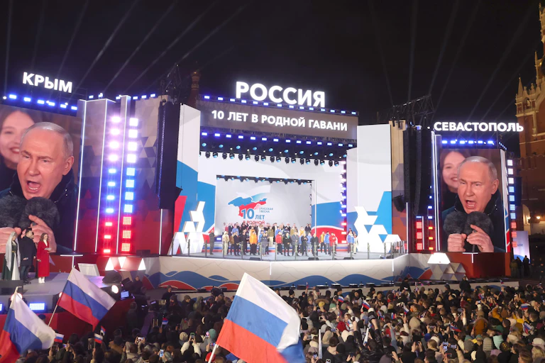 Vladimir Putin on a stage addressing a large crowd.