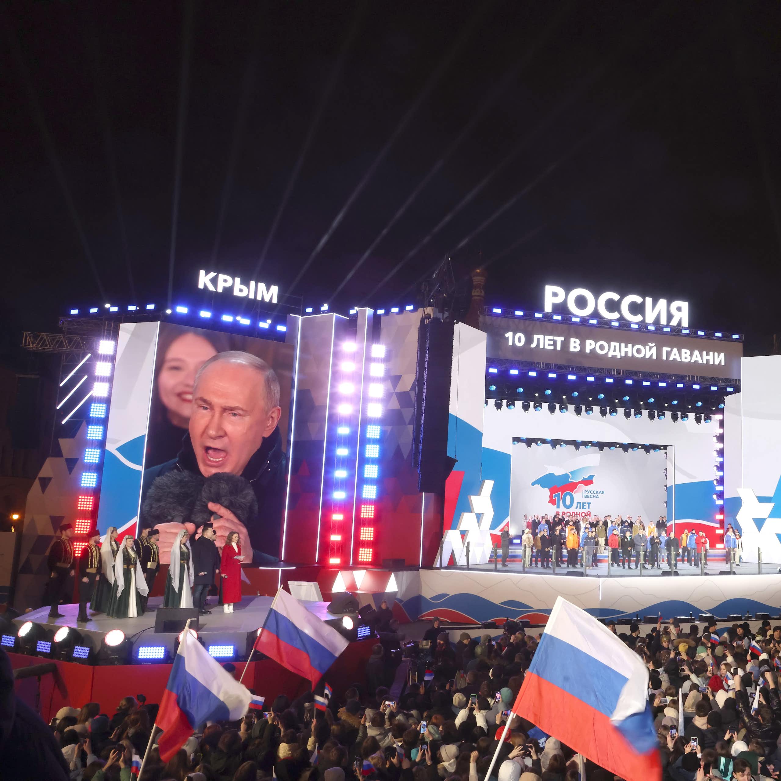 Vladimir Putin on a stage addressing a large crowd.